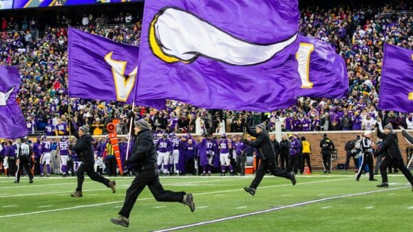 people running and holding Minnesota Vikings flags in green field